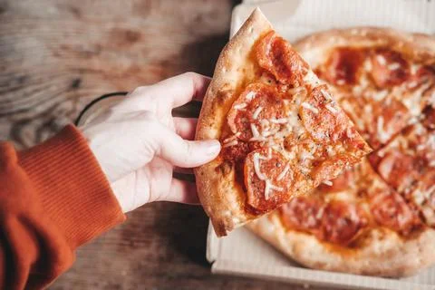 Large slice of pepperoni pizza in hands, close-up. Delicious Italian snack. P Stock Photos