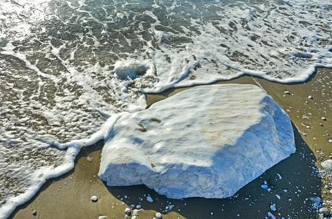 A large smooth block of white marble in the sand on the coast. Selective focu Stock Photos