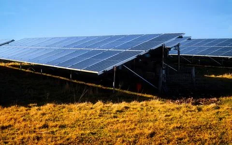 Large solar panel array installation on a grassy hillside under a clear blu.. Stock Photos