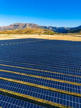 Large solar panel array in an open field under a clear blue sky near mounta.. Stockfoto's