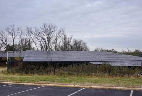 Large solar panel array in an overgrown field behind a chain link fence Stock Photos