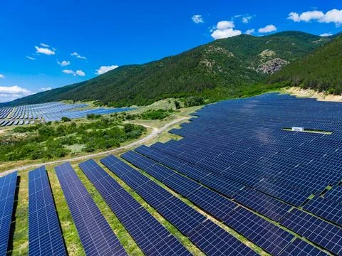 A large solar panel field placed on a hillside close to a mountain range. The Stock Photos