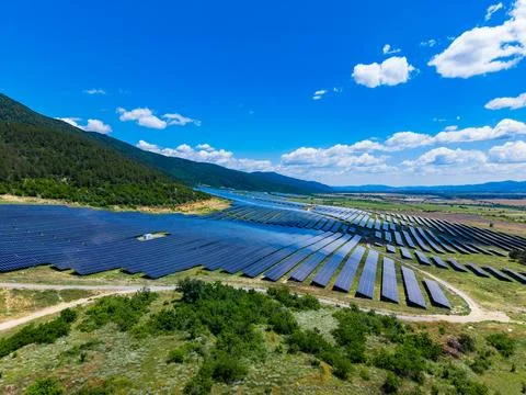 Large solar panel fields stretch across a landscape with a lake in the backgr Stock Photos