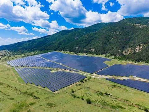 Large solar panel installation spreads across flat land surrounded by mountai Фото
