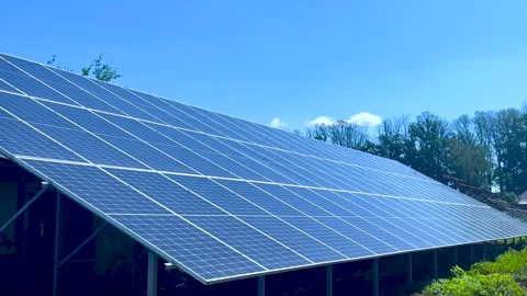 Large solar panels are installed on the ground against a blue sky. In the Stock Footage 277727825