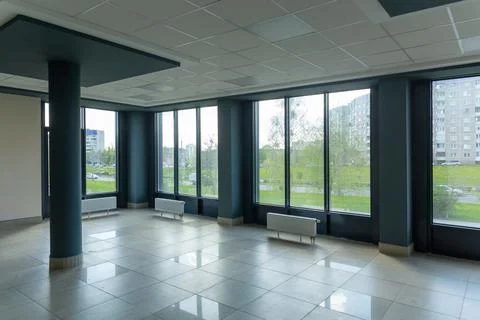 A large, spacious, empty room with huge windows and floor-mounted central hea Stock Photos