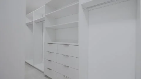 Large spacious empty walk-in closet with white cabinets, drawers, and holders Stock Footage 249520883