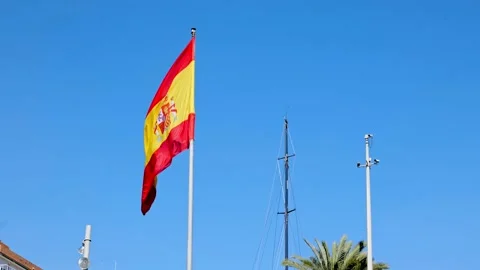 A large Spanish flag flies under a blue sky at the port of Alicante. Stock Footage 153239026
