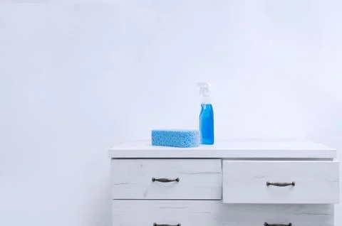 Large sponge and cleaning spray on a gray chest of drawers against a white wa Stock Photos
