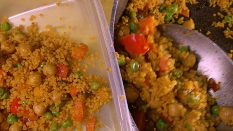 A large spoon transferring vegetable couscous from a pan to a plastic container. Stock Footage 291286812