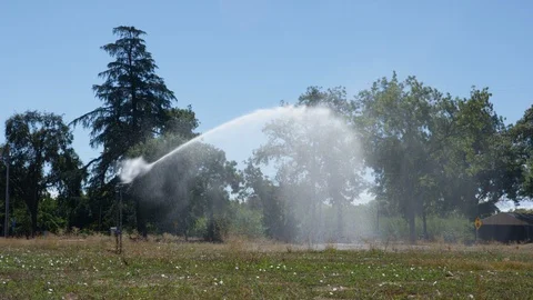 Large sprinkler system spraying water stream watering open field by road B Stock Footage 112883978