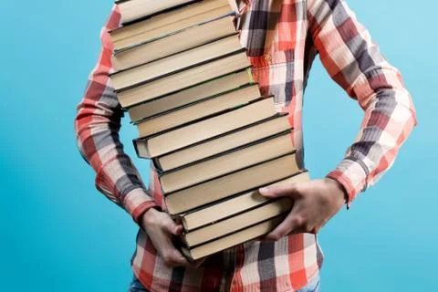 A large stack of books is hardly held in the hands of a young girl Stock Photos