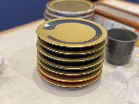A large stack of empty gold-colored sushi plates with a plastic grey cup at a Stock Photos