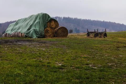 Large stack of round hay bales an a field with an old trailer next to it. Stock Photos