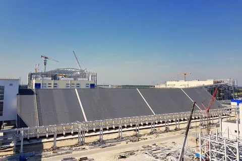 A large structure rises in the background, with cranes and scaffolding presen Photos