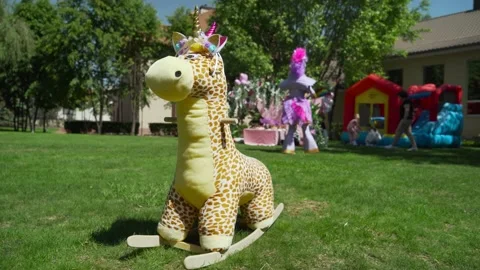 A large stuffed giraffe toy is lying on the lawn. A children's party is taking Stock-Footage 220904054