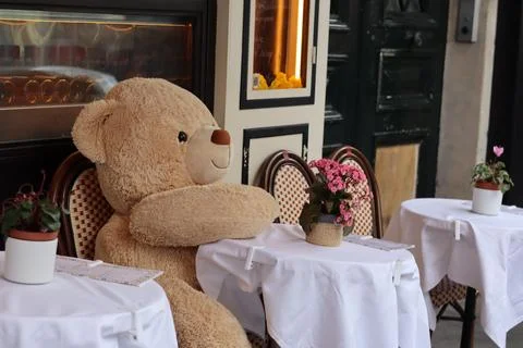 Large stuffed teddy bear sitting at a cafe table in a quaint outdoor dining.. Stock Photos
