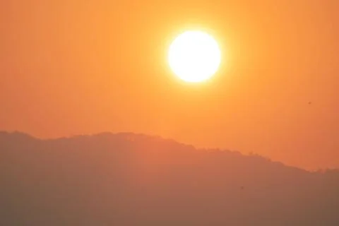 A large sun is in the sky, with a mountain range in the background Stock Photos