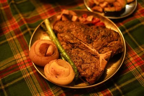 Large T-Bone Steak and Vegetables on a Christmas-Themed Plaid Tablecloth Stock Photos