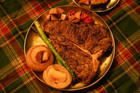 Large T-Bone Steak and Vegetables on a Christmas-Themed Plaid Tablecloth Stock Photos