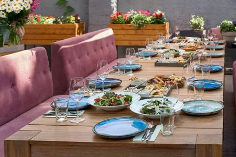 Large table on the sun terrace waiting for guests. Blue plates and food on th Stock Photos