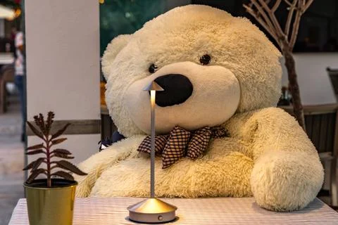 A large teddy bear sitting at a table in a restaurant, a teddy bear on a ch.. Stock Photos