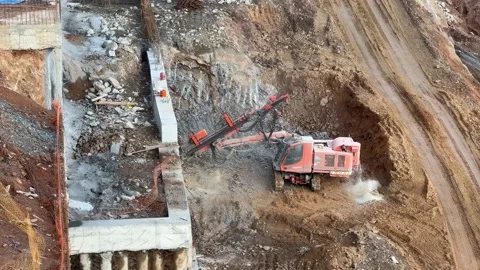 A large, tracked orange drilling rig is boring into a rock surface on a Stockbeeldmateriaal 336042203
