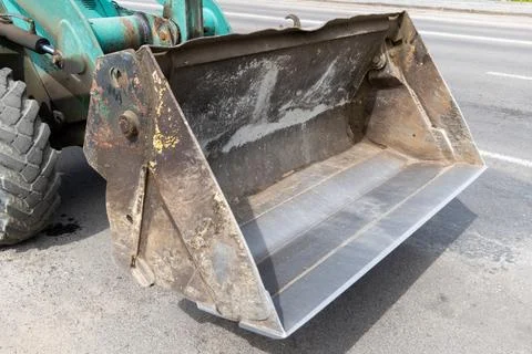 A large tractor bucket is parked on a construction site close to the road. .. Stock-Fotos