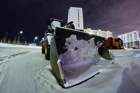 Large tractor loader bucket with snow inside modern city street Stock Photos