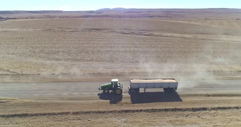Large tractor pulling crop laden trailer along dusty farm road aerial shot Stock-Footage 93825248