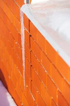 A large transparent icicle on the background of a red brick wall hangs from t Stock Photos