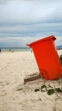 Large trash can resting on the beach sand. Stock Photos