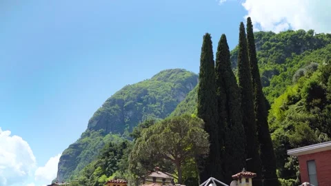 Large trees in front of tree covered mountain with italian house roofs Stock Footage 277029258