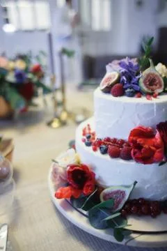 A large two-tiered cake decorated with fruit and fresh flowers. Stock Photos