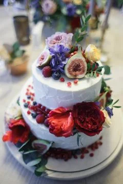 A large two-tiered cake decorated with fruit and fresh flowers. Stock Photos