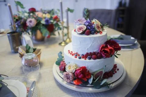 A large two-tiered cake decorated with fruit and fresh flowers. Stock Photos