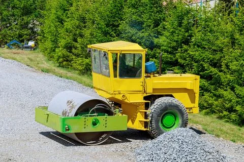 A large vibrating road roller compacts the gravel into the ground. Stock Photos