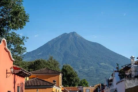 Large volcano peak covered in trees towering above ancient city structures .. Stock Photos