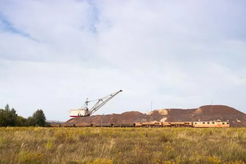 A large walking excavator forms dumps of rock delivered by freight train from Stock Photos