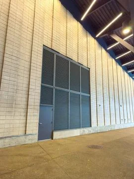A large wall made of blocks shows a door on one side. Horizontal metal slats  Stock Photos