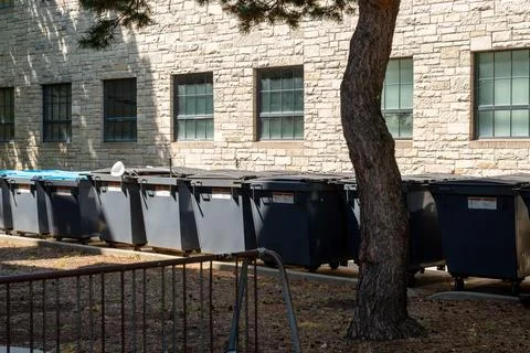 Large waste bins lined up outside a building, symbolizing urban waste managment Foto stock