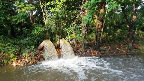 Large water pipe discharging liquid waste into a small pond Stock Footage 75117397