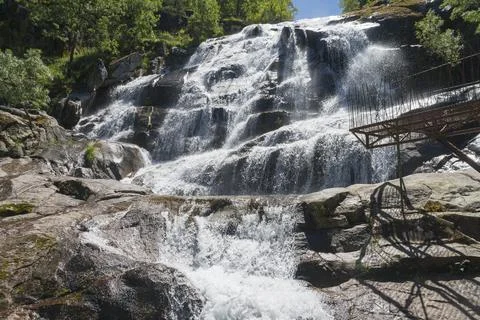 A large waterfall flows over rocks with a parapet in the foreground, surrounded Foto stock