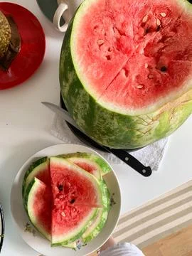 A large watermelon is cut open on a table, revealing its red flesh inside. .. Stock Photos