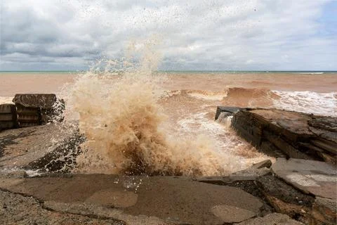 A large wave crashes into splashes on a breakwater during a storm Stock Photos