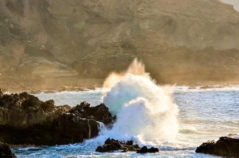 A large wave is crashing into the rocks, creating a powerful and dramatic sce Stock Photos