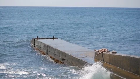 Large waves break on a concrete breakwater. A plump woman in a swimsuit lies on Stock Footage 115069377