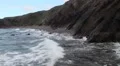 Large waves crashing against rocks and mountains at the beach shoreline HD Footage