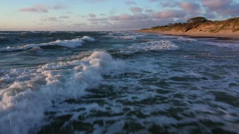 Large waves with foam roll on hilly ocean beach at sunset Stock Footage 148782295