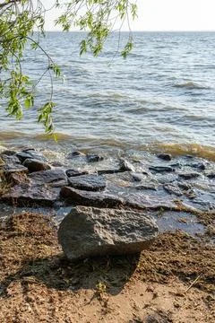 Large weathered grey stone sits on the damp sandy shore near rippling lake .. 库存照片